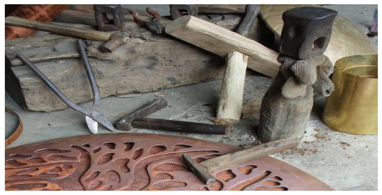 Copper and brass sheet metal, hammers, and hand tools on a workbench in the Bronze Age shop